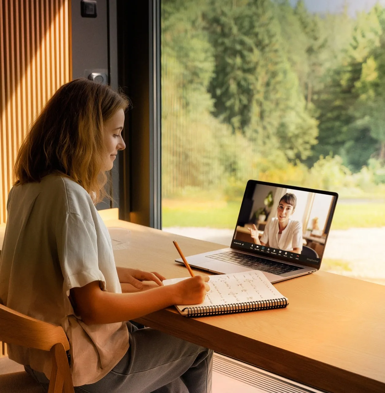 A student attending a remote learning session via a RingCentral video call on a laptop with a view of a forest through the window.