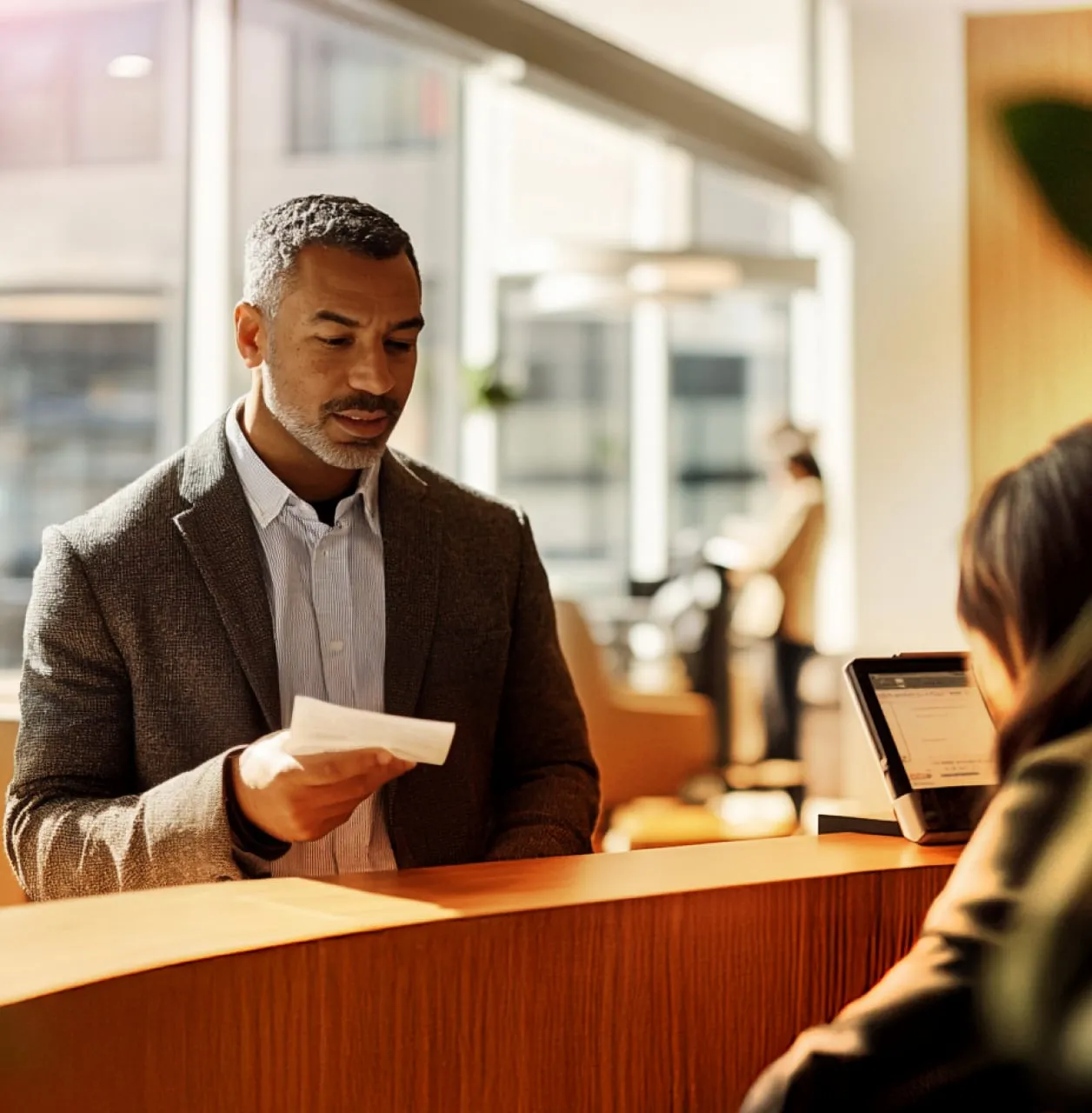 A male customer consultant in a grey blazer assisting a client at a modern financial services branch desk.