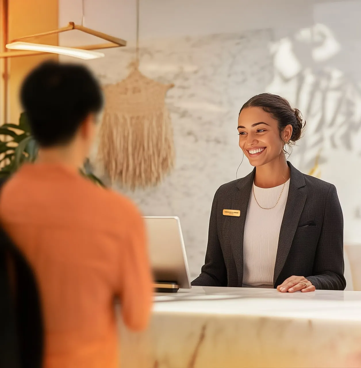 Receptionist in a suit smiling at a person across a counter.