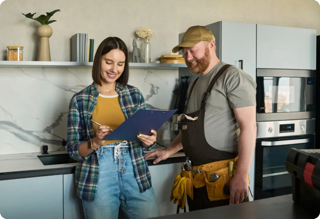 Woman and handyman smiling while reviewing renovation checklist in modern kitchen.