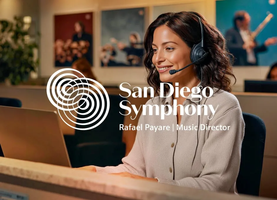 A smiling woman in a headset works on a laptop in an office decorated with portraits of musicians.