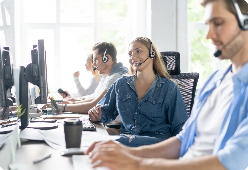 A diverse group of people working at desks in a busy call center, engaged in phone conversations and using computers.