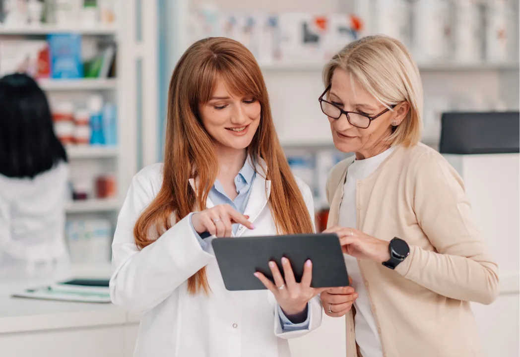 Two women in a pharmacy examining a tablet together, discussing its features and benefits.